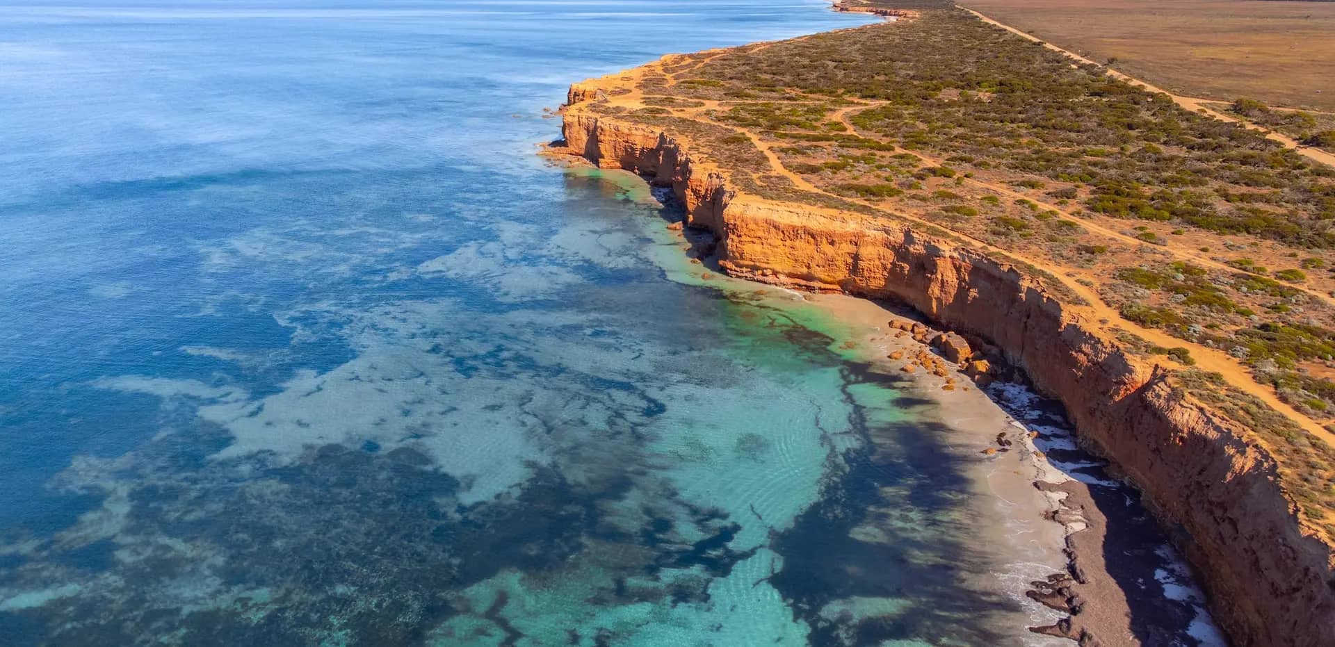 Aerial view of the orange limestone cliffs and clear turquoise reef waters of the Eyre Peninsula coast