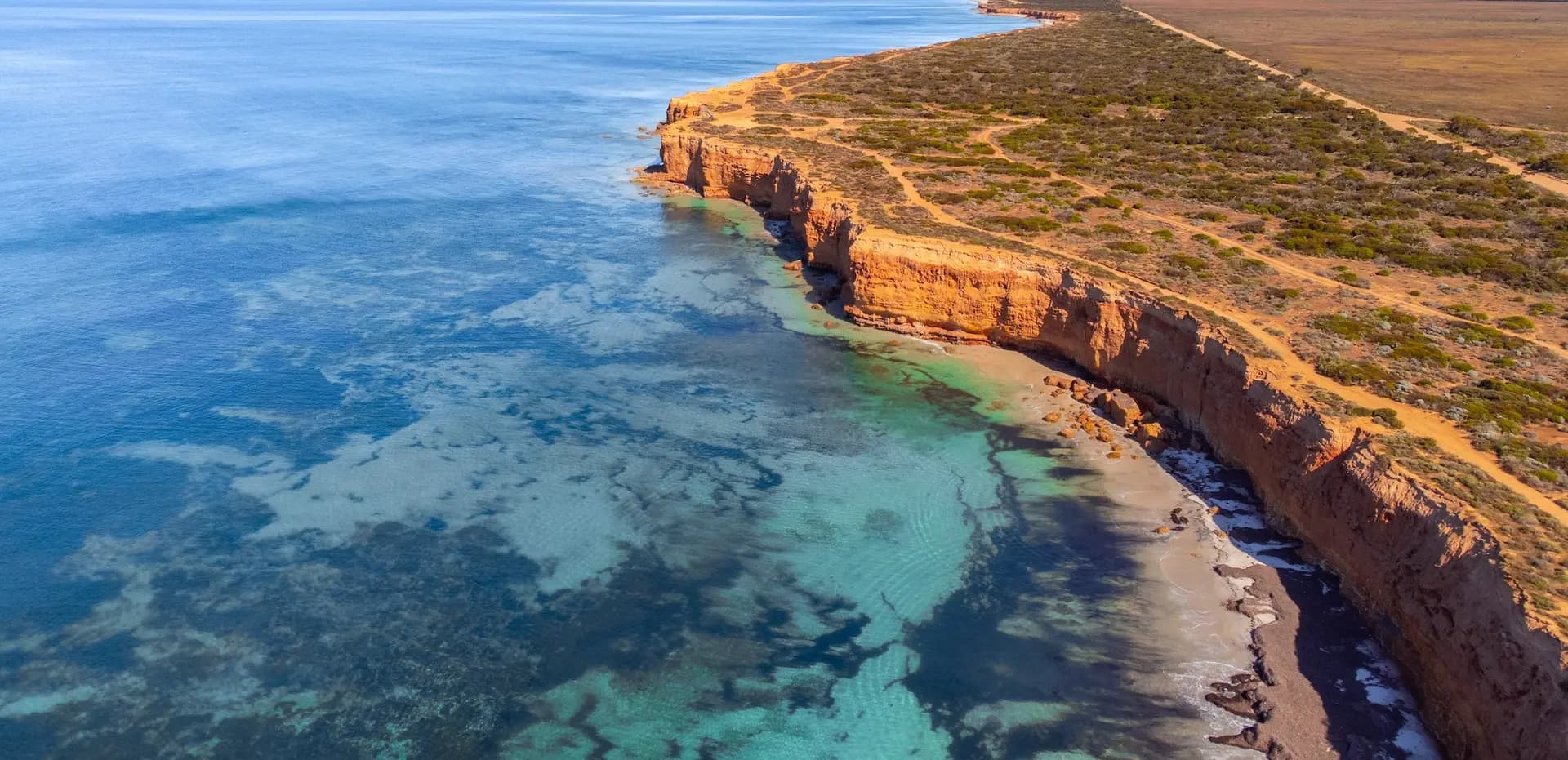 Aerial view of the orange limestone cliffs and clear turquoise reef waters of the Eyre Peninsula coast